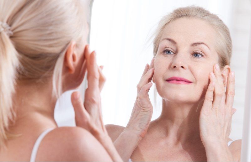 Older woman looking in mirror and touching cheeks