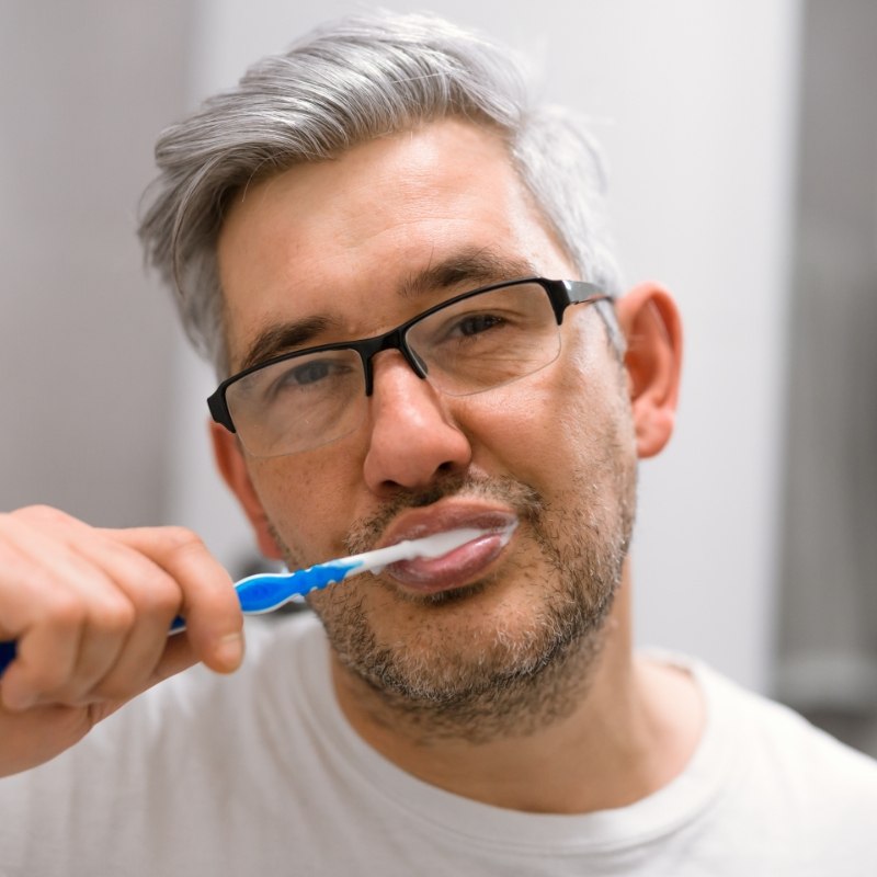 Older man with glasses brushing his teeth