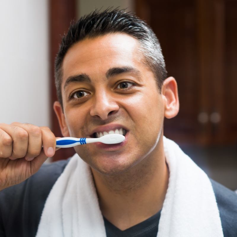 Man with towel around neck brushing his teeth