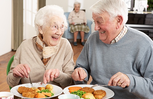 A man and woman smiling and eating with dental implants