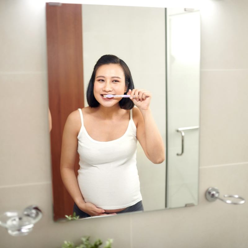 Woman in white shirt brushing teeth in mirror