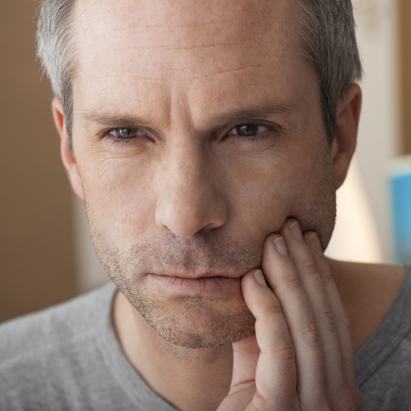 Man feeling his jaw looking concerned