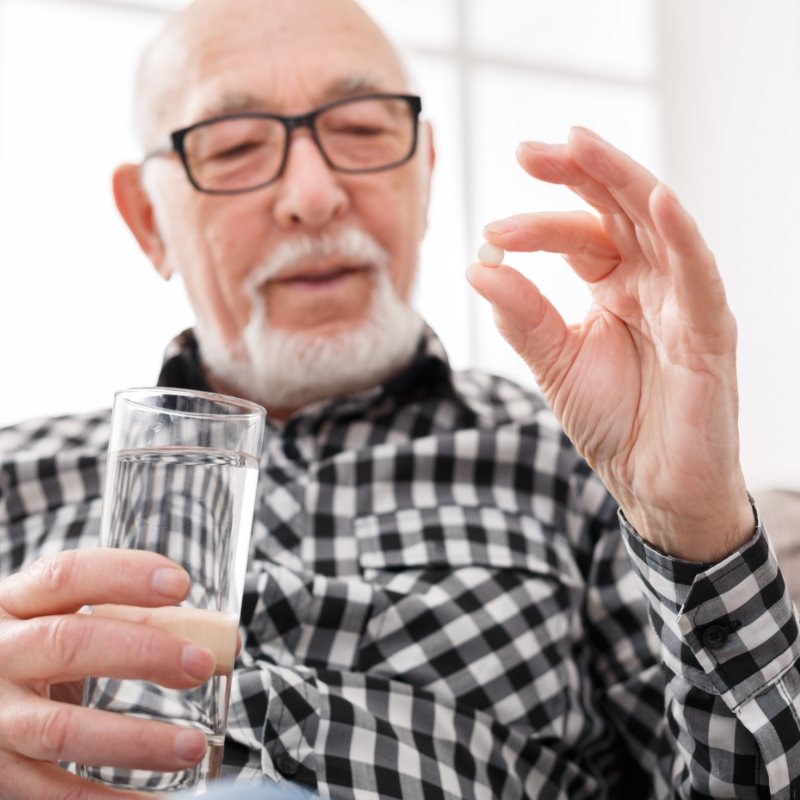 Man with glasses holding pill and glass of water