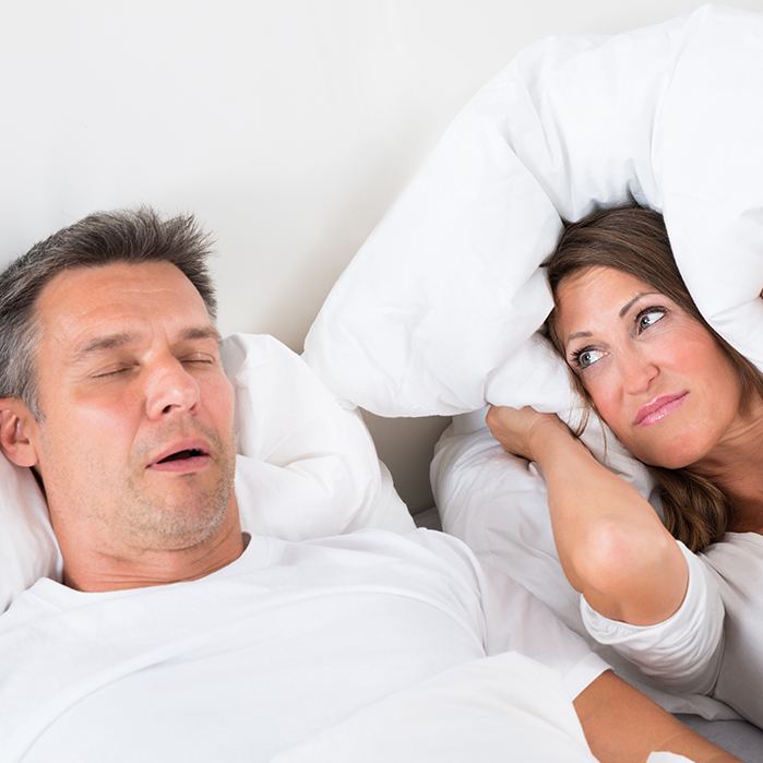 Man snoring while woman covers ears with pillow