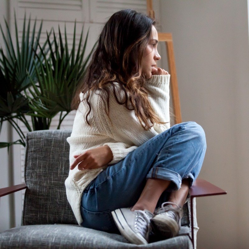 Woman in sweater curled up looking worried